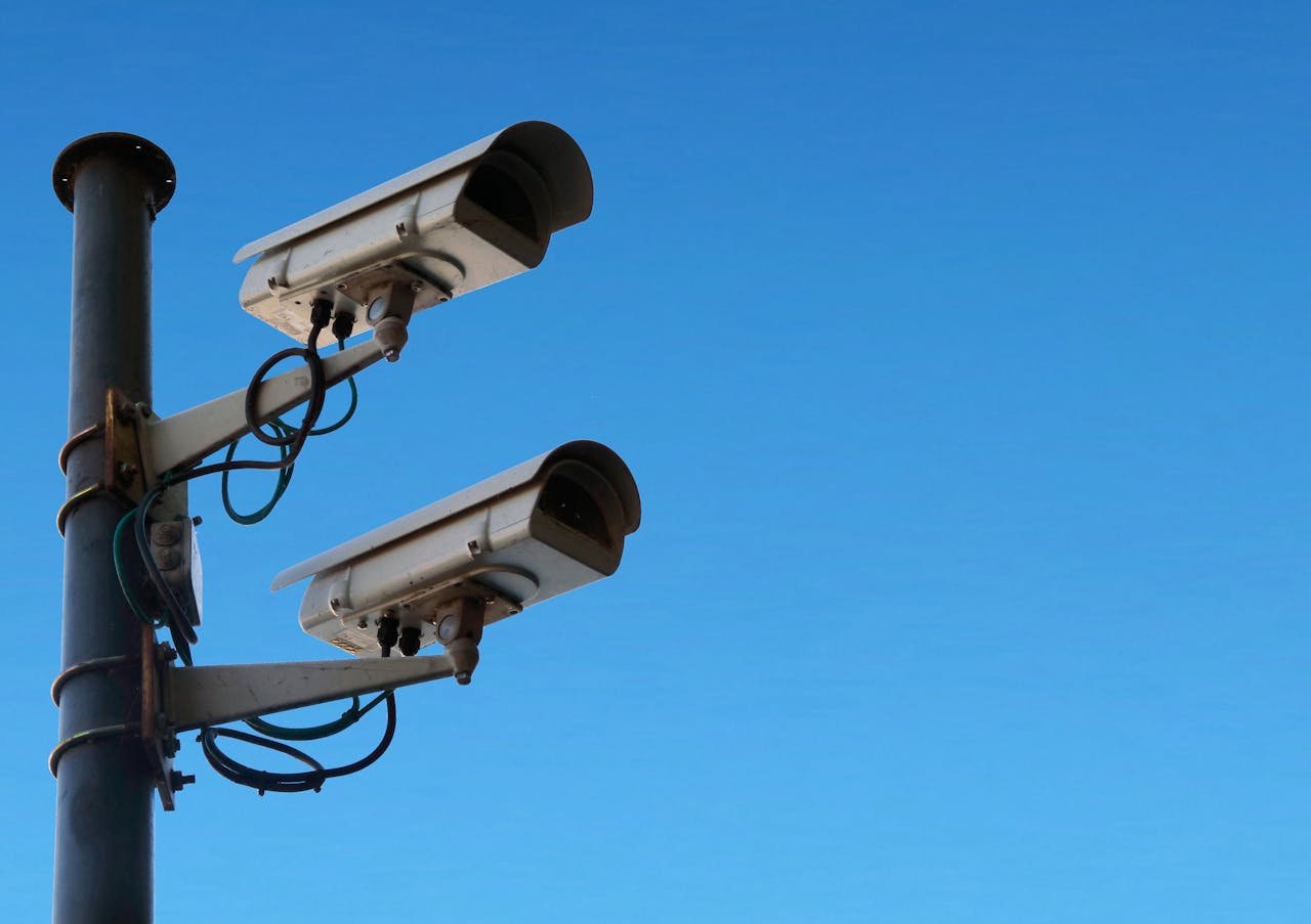 services-03 Two security cameras mounted on a pole with a bright blue sky as the backdrop.