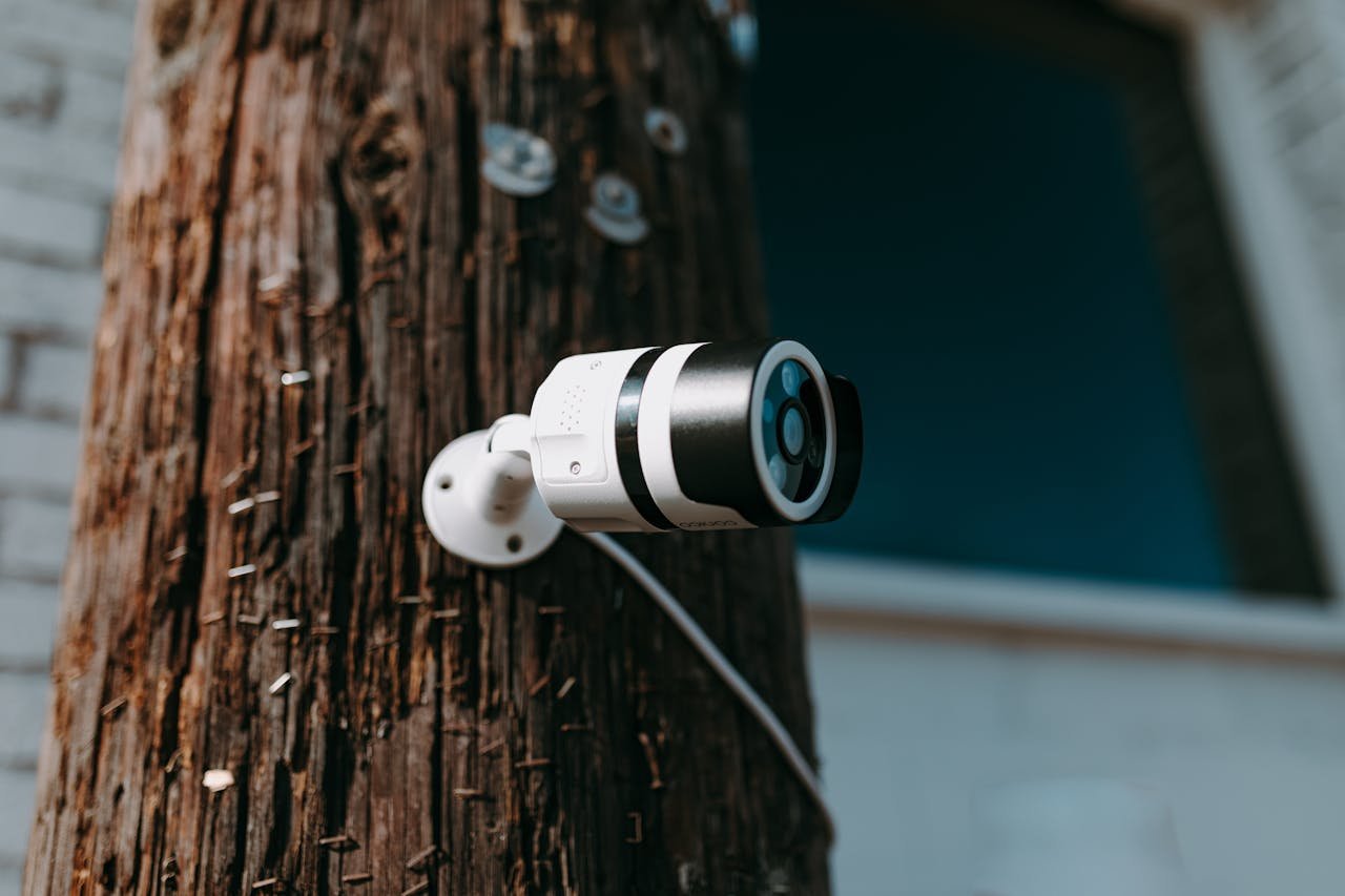 heros-img Close-up of a modern security camera mounted on a wooden post outdoors.